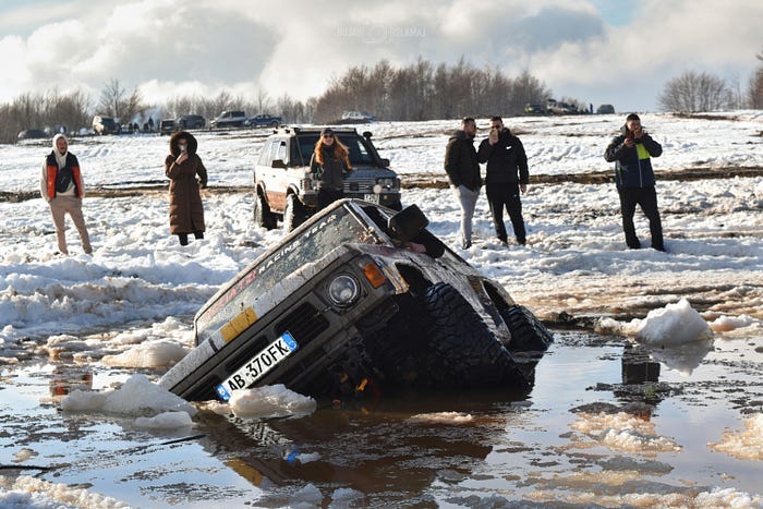 People standing around in the winter on top of snow. They’re staring at an SUV that’s half-submerged in the water, wondering what they should do.. People standing around in the winter on top of snow. They’re staring at an SUV that’s half-submerged in the water, wondering what they should do..