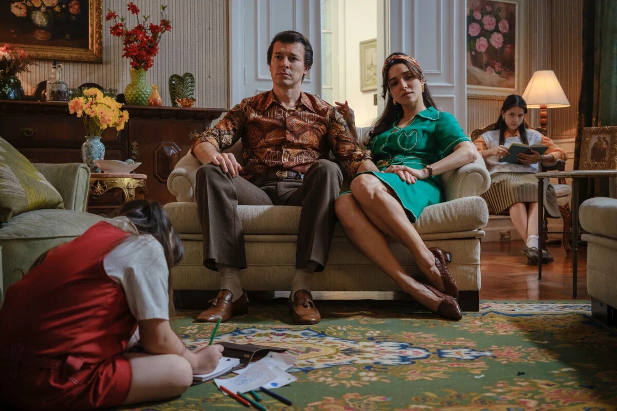 Silvio Santos, a esposa Cidinha e duas filhas numa sala de estar luxuosa e cheia de flores. Estão vestidos com roupas que podem ser do fim dos anos 60 e começo dos anos 70. Silvio Santos, a esposa Cidinha e duas filhas numa sala de estar luxuosa e cheia de flores. Estão vestidos com roupas que podem ser do fim dos anos 60 e começo dos anos 70.