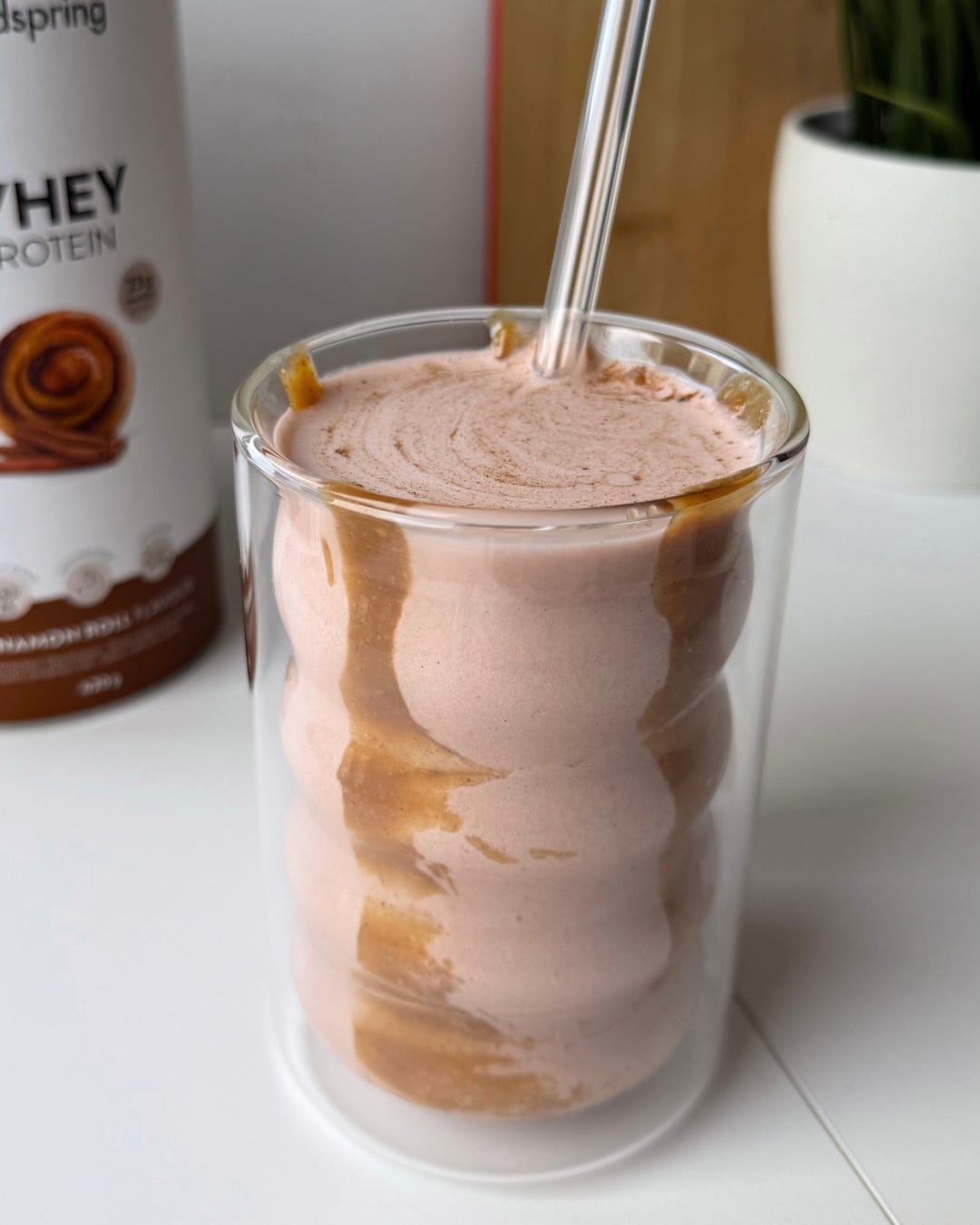 A creamy cinnamon roll protein smoothie in a glass, with a marble almond butter effect and topped with a sprinkle of cinnamon and granola.