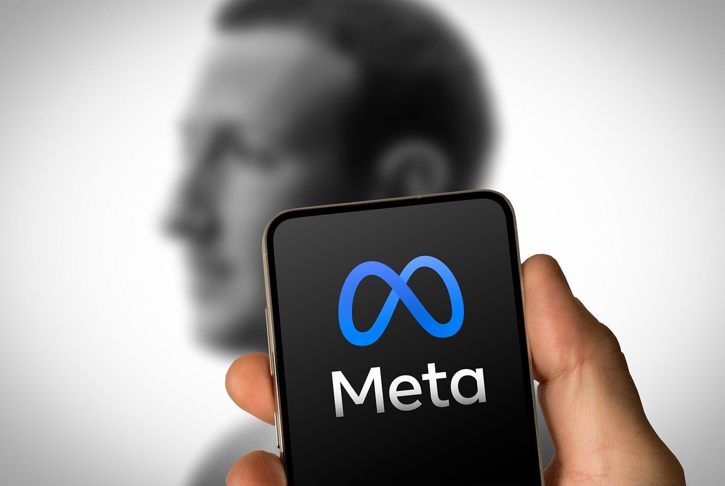 Someone holding a phone with the Meta logo on the screen and Mark Zuckerberg in a blurry background Someone holding a phone with the Meta logo on the screen and Mark Zuckerberg in a blurry background