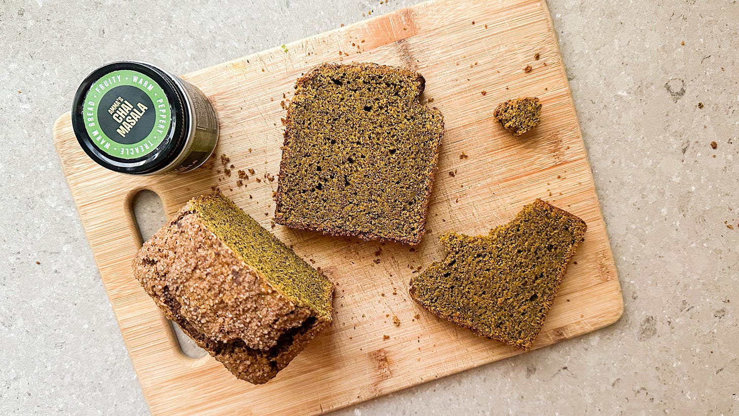 Slices of gluten-free pumpkin bread on a wooden cutting board with a bottle of chai masala spices.