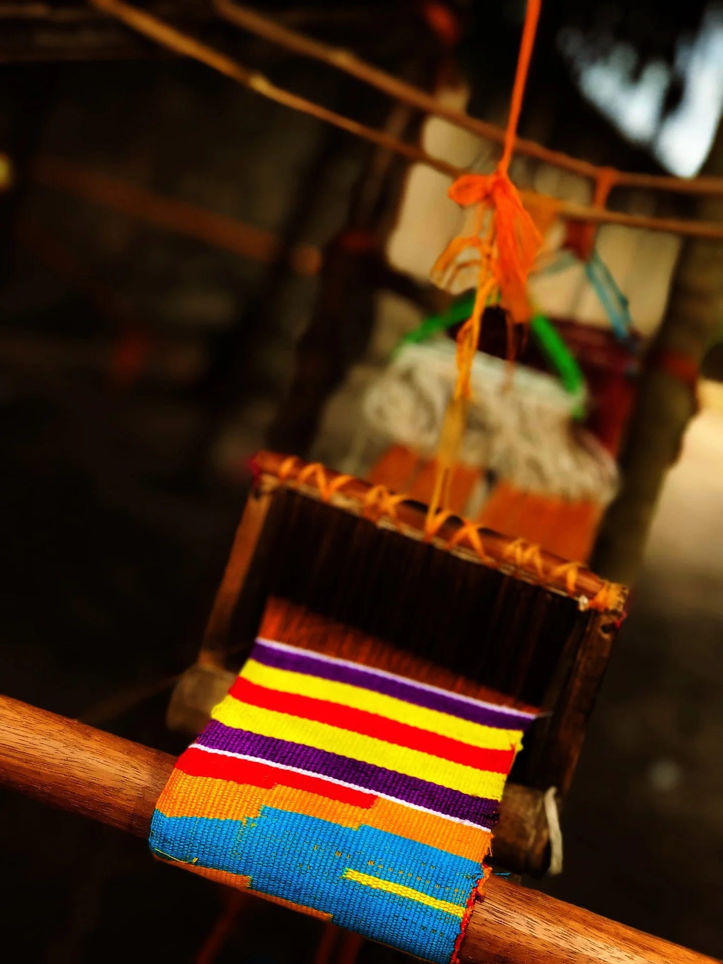 A narrow strip of Kente cloth being woven on a loom.
