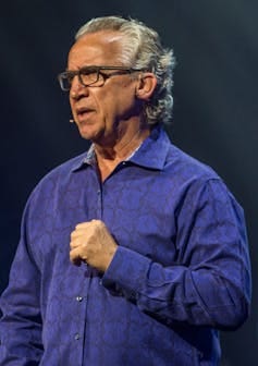 A gray-haired man wearing glasses and a blue shirt. A gray-haired man wearing glasses and a blue shirt.