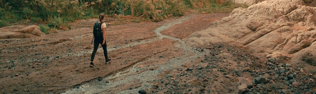 a man walking down a dirt road next to a mountain