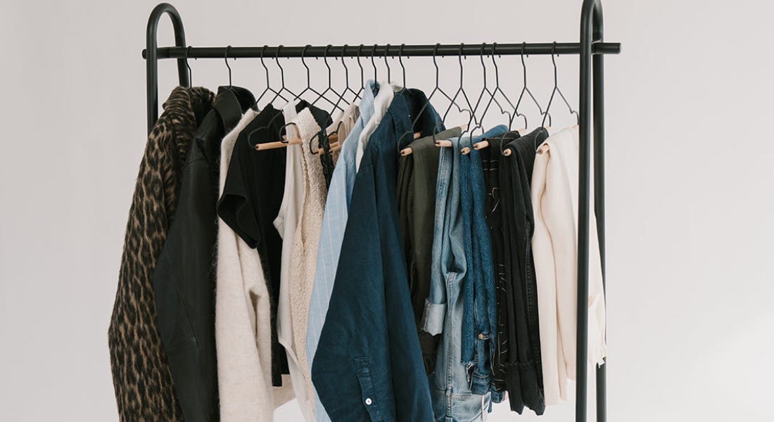 A black clothes rail with jackets, cream tops, blue jeans and shirts, and trousers hanging from it A black clothes rail with jackets, cream tops, blue jeans and shirts, and trousers hanging from it