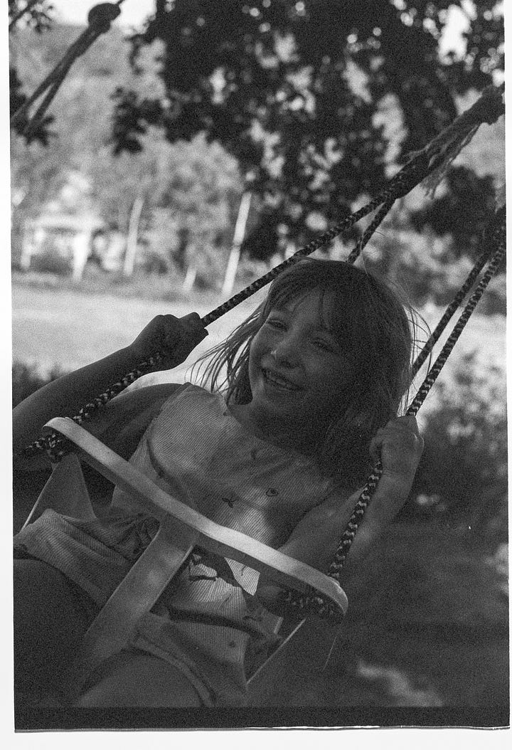A child swings in a plastic baby swing, laughing and hair flying.