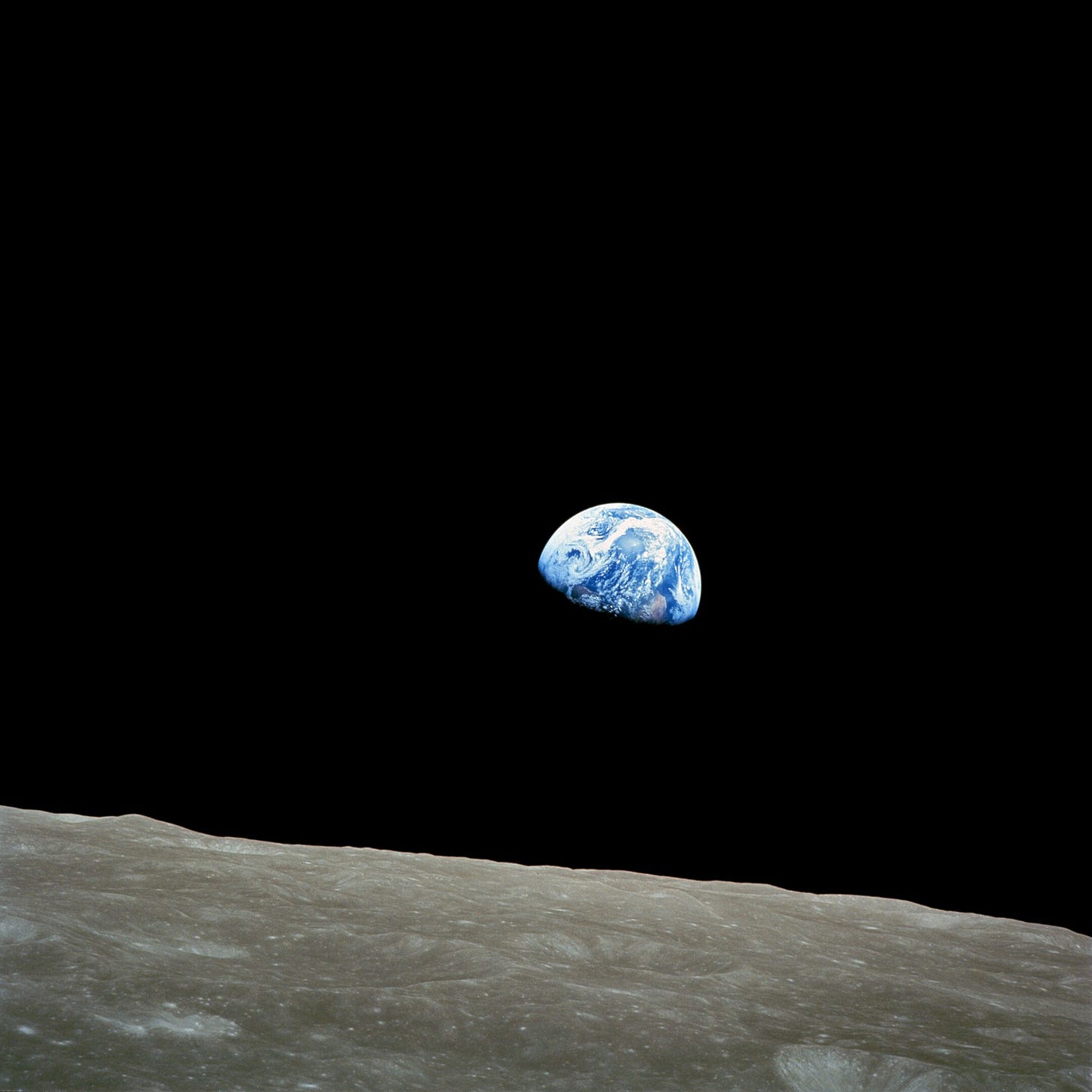 Deep black space in background. Halfmoon shape of blue-swirled earth center. Gray moonscape below. This is Earthrise taken by astronaut William Anders on Dec. 24, 1968.