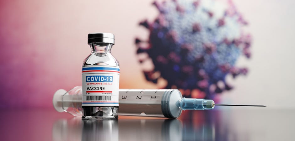 A COVID-19 vaccine vial and syringe beside an illustrated coronavirus particle on a reflective surface.