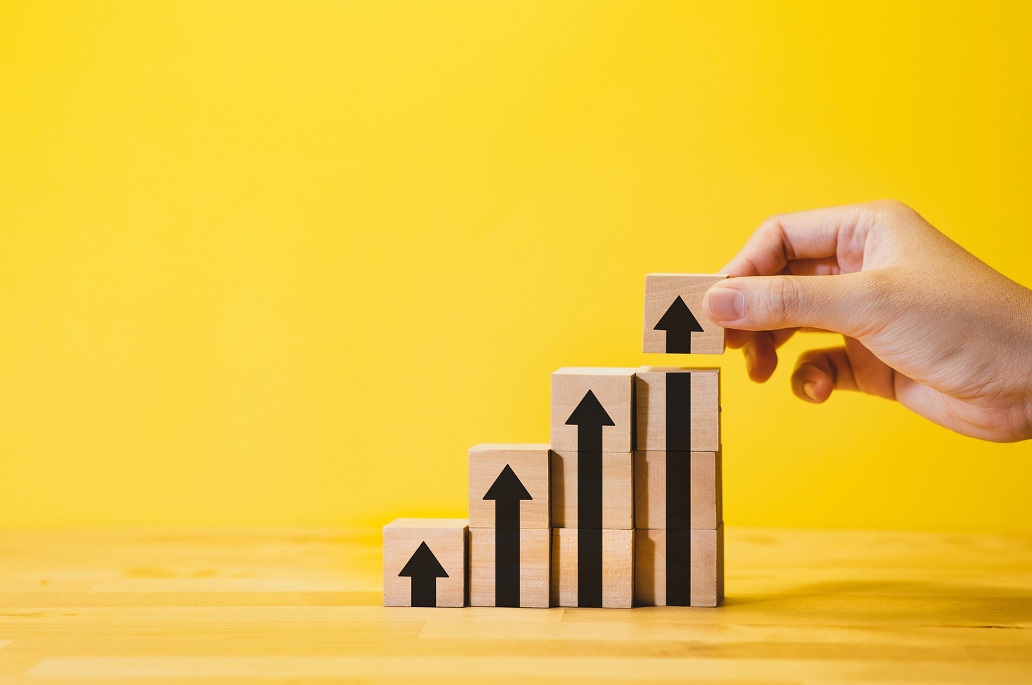 Tiered building blocks with arrows pointing up against a yellow background