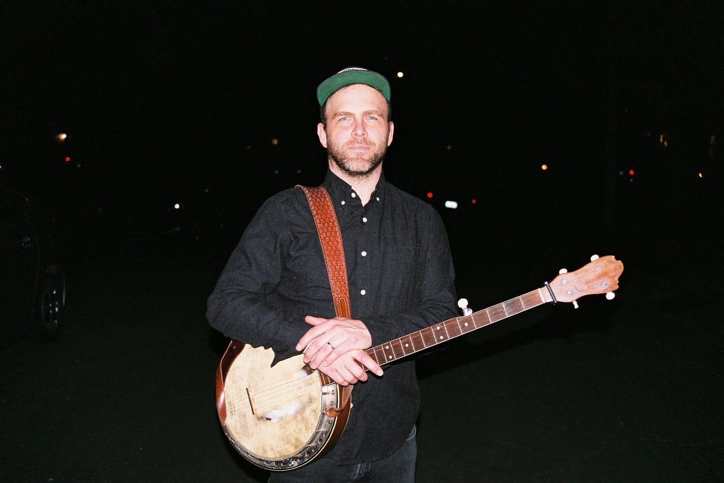 A photo of Joseph Decosimo taken with a powerful flash. He is resting his hands on his banjo, and looks very dignified!