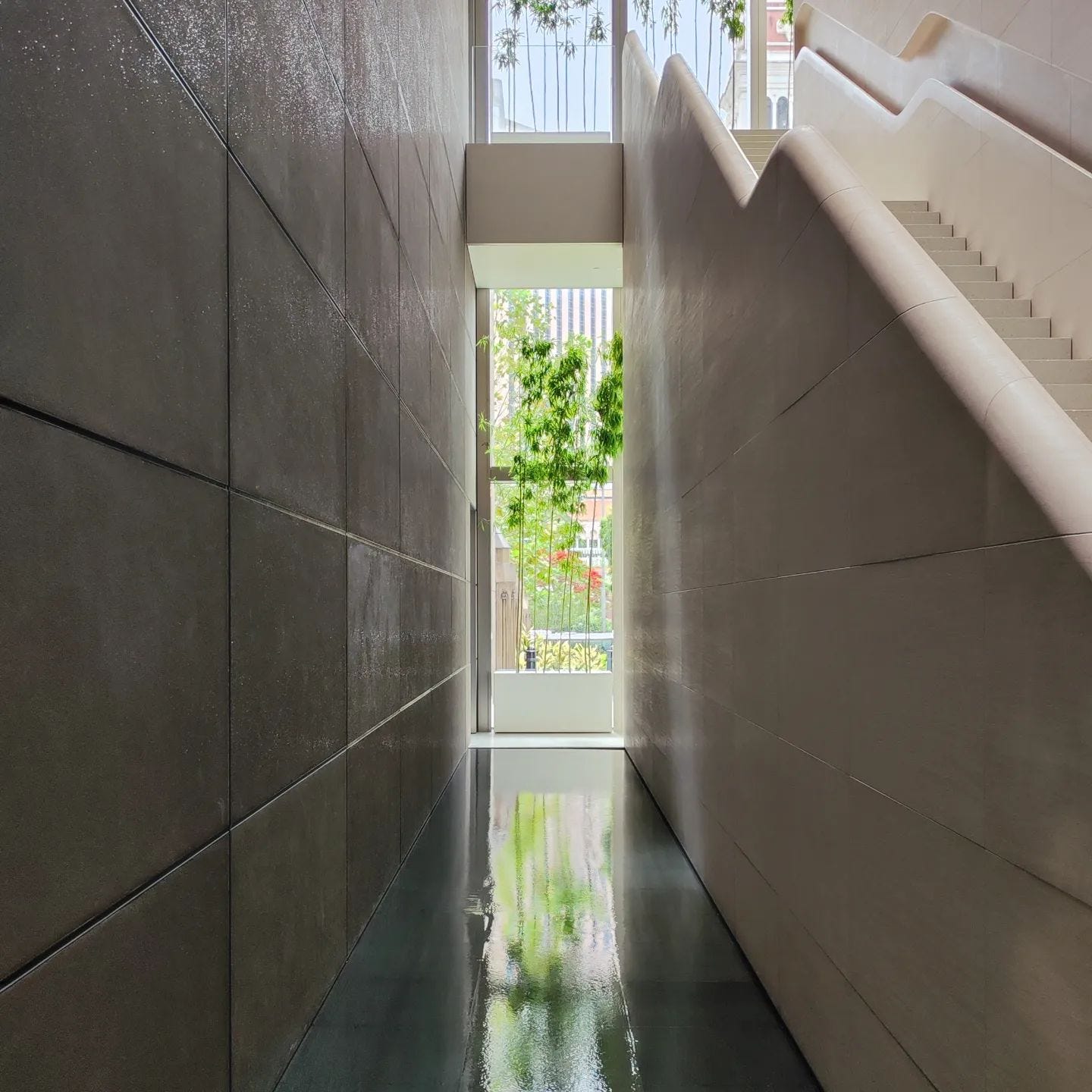 A narrow perspective between the wall and sculptural staircase at Apple Cotai Strip. Bamboo planters sit in the distance.