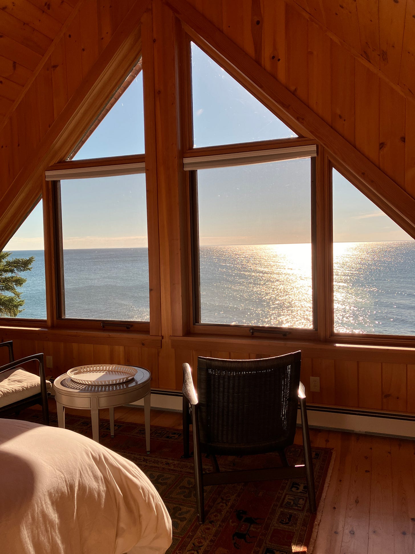 Large windows of an A-frame cabin look out over Lake Superior's massive expanse of water at sunrise.