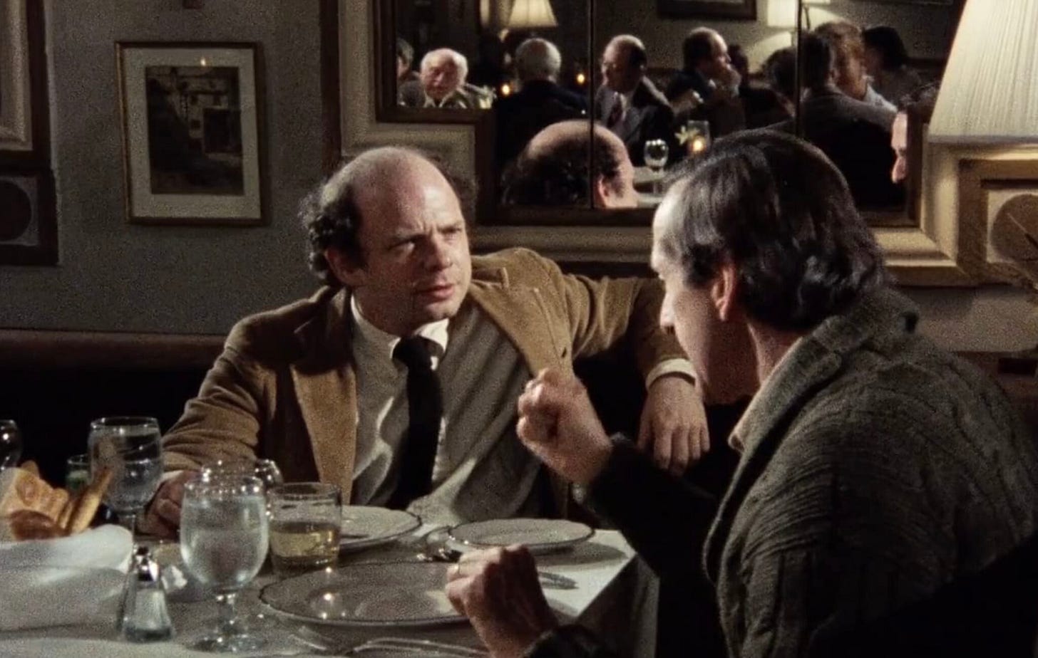 Screencap from My Dinner With Andre. Wallace Shawn listens, his arm resting on the back of the chair. Andre is telling a story. No food on their plates. Screencap from My Dinner With Andre. Wallace Shawn listens, his arm resting on the back of the chair. Andre is telling a story. No food on their plates.