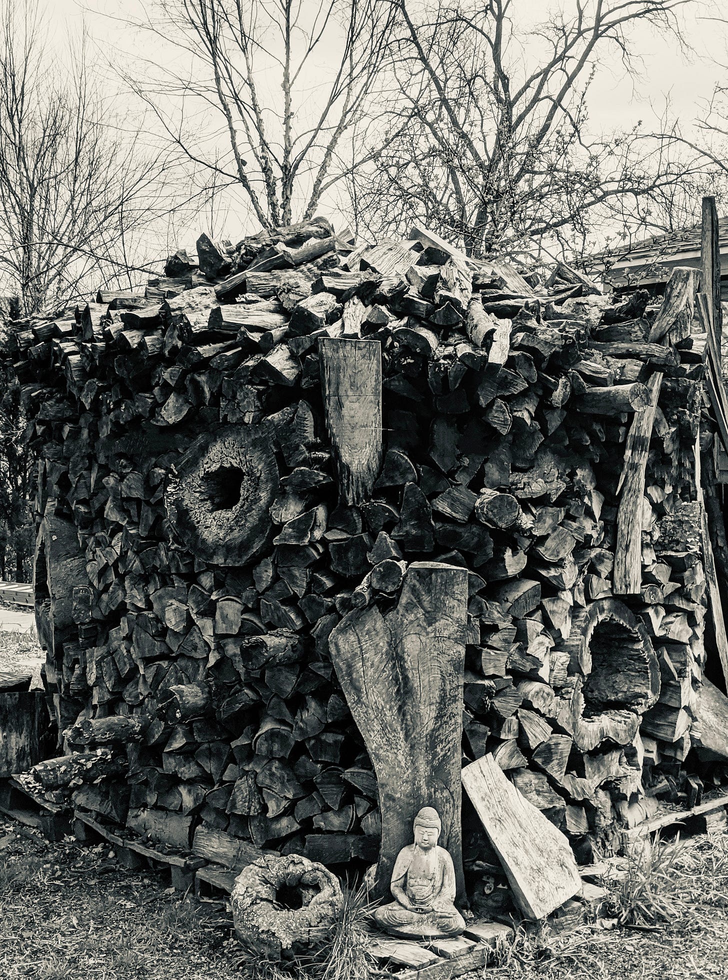A winter stack of firewood with a small Buddha statue resting at the base.