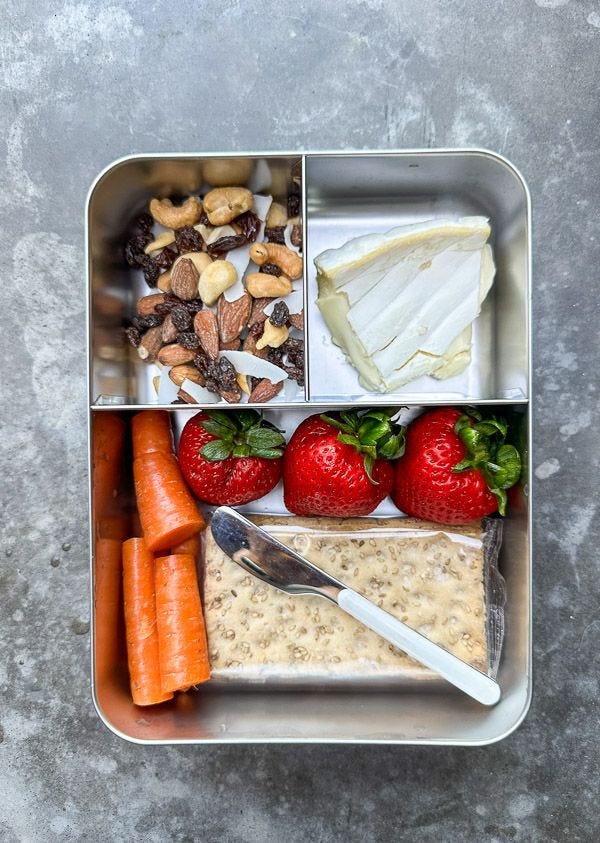 This may contain: a bento box with carrots, crackers, yogurt and fruit