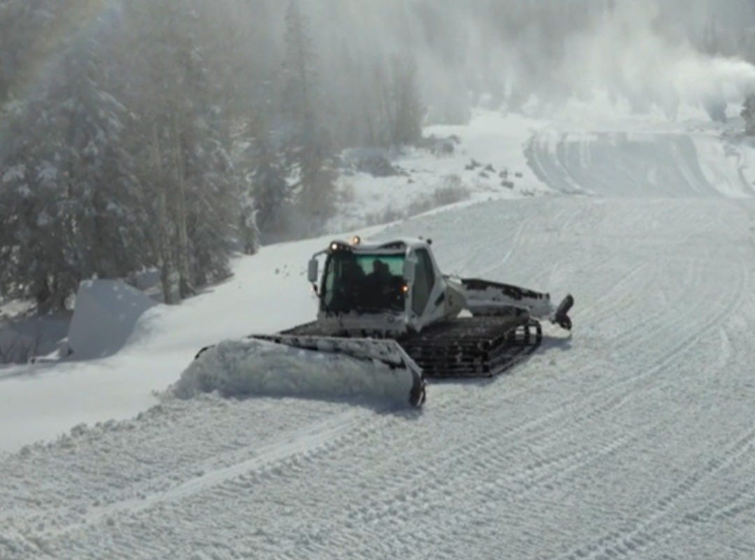 Photo of a snow groomer pushing snow on a ski trail.