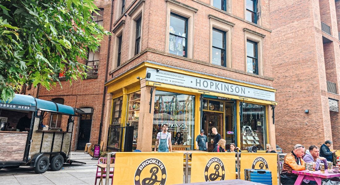 A yellow shop with people sat outside of it and brick material around it