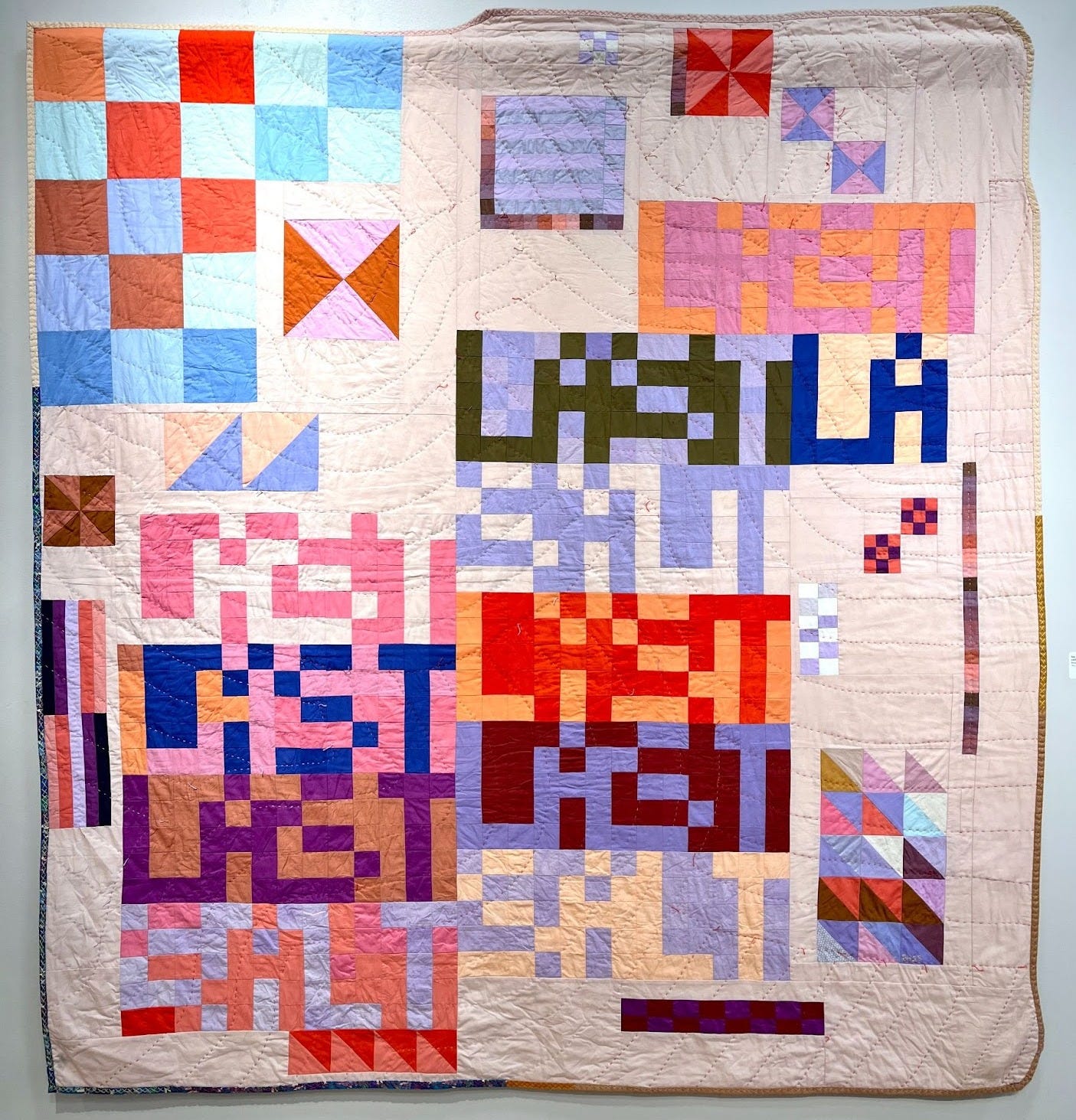 An improv quilt hanging on a wall. The vibe is disjointed with the words “LAST” and “SALT” pieced together in pixelated grid font, surrounded by geometric shapes in random pinks, purples, blues, and peaches, all on a light peach background. Hand stitched in fluid parallel lines. The right 2 corners are rounded, and the top edge isn’t completely straight. 