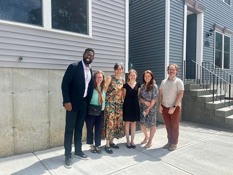 Photo of elected officials and Habitat homebuyers during a ribbon cutting, holding a large symbolic check from the City of Albany and a photo of staff from Community Preservation Corporation in front of Habitat homes.