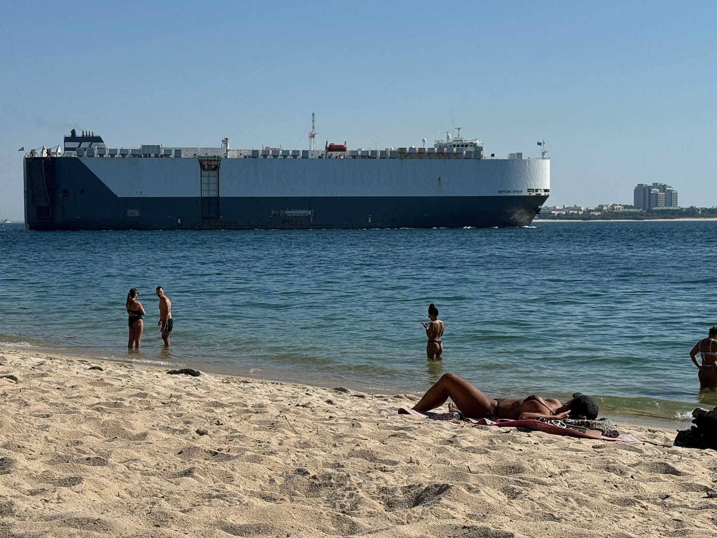 A giant tanker ship passes sunbathers on a beach. A giant tanker ship passes sunbathers on a beach.