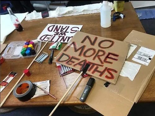 Photo of a table littered with art supplies and cardboard for protest sign preparation; two completed signs read "UNITED WE STAND" and "NO MORE DEATHS" Photo of a table littered with art supplies and cardboard for protest sign preparation; two completed signs read "UNITED WE STAND" and "NO MORE DEATHS"