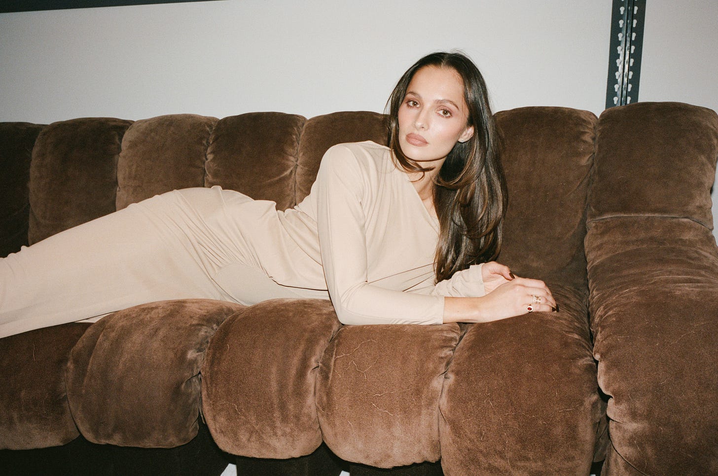 Pia Mance in a neutral dress on a brown sofa. 