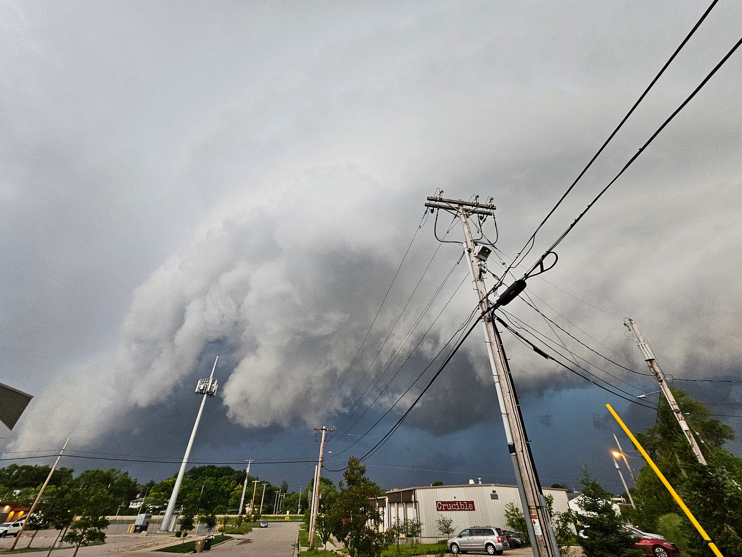 A large wall cloud looms over darker skies. Underneath, a city street and utility poles line the warehouse where the nightclub Crucible is housed.