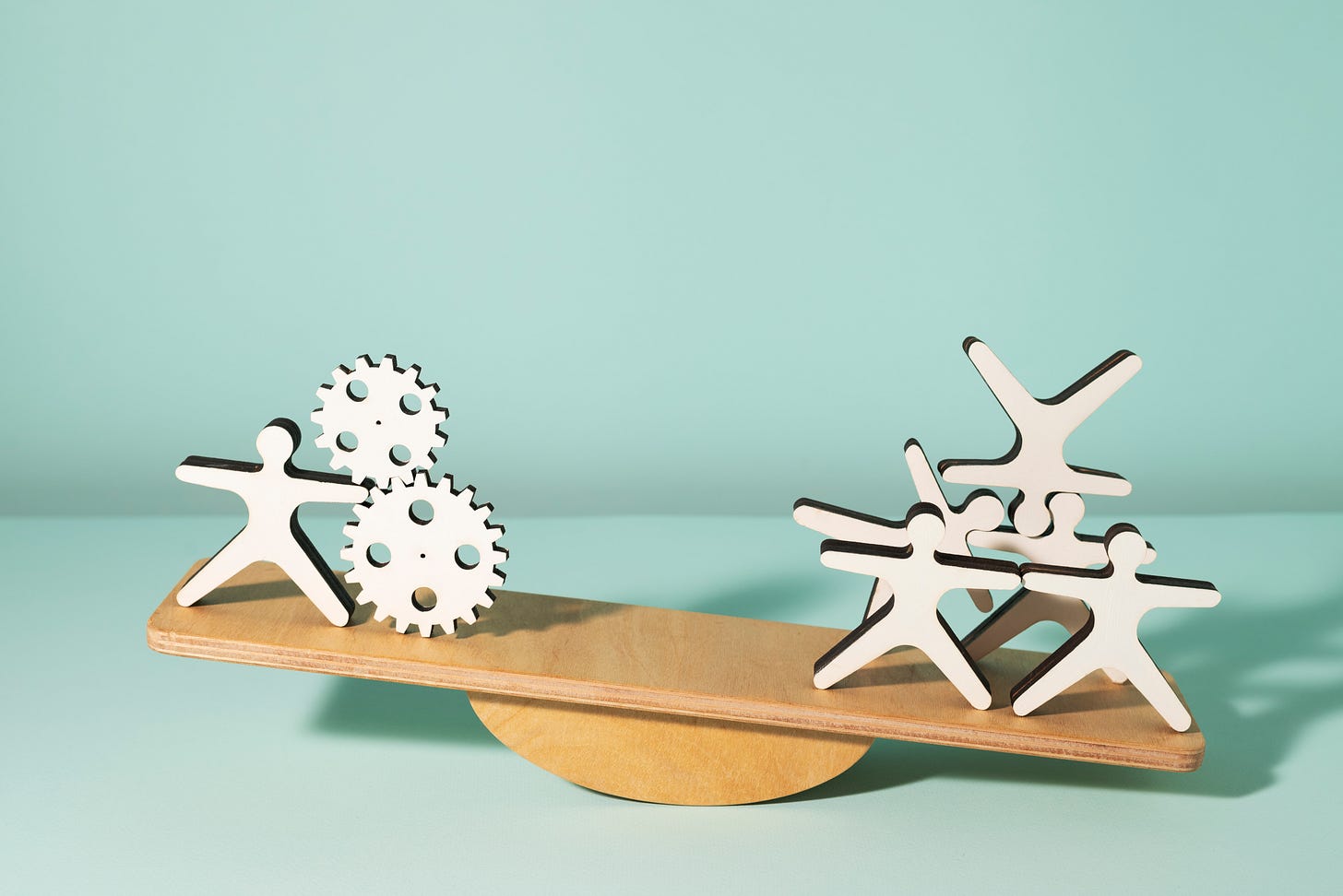 Cutouts of people and machine cogs on a teeter-totter.