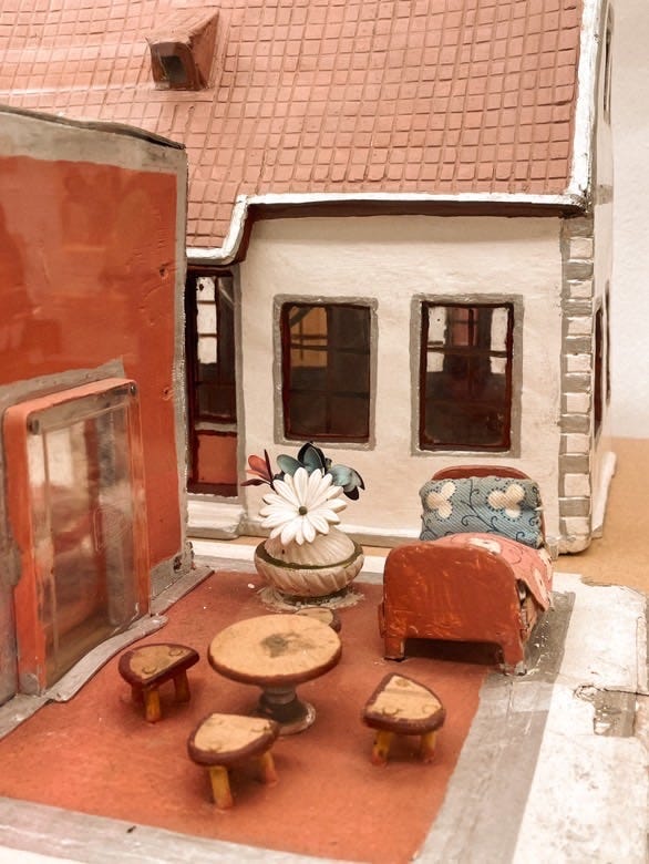 1) A forest of trees coated in ice after freezing rain at dawn. 2) Small red & white clay figurines of buildings, homes, and furniture. 3) A laminated printout of a hand with a cancel sign through it, sitting on the seat of a red & orange floral fabric chair. 4) Wooden double doors with ornate iron grating over stippled glass windows.