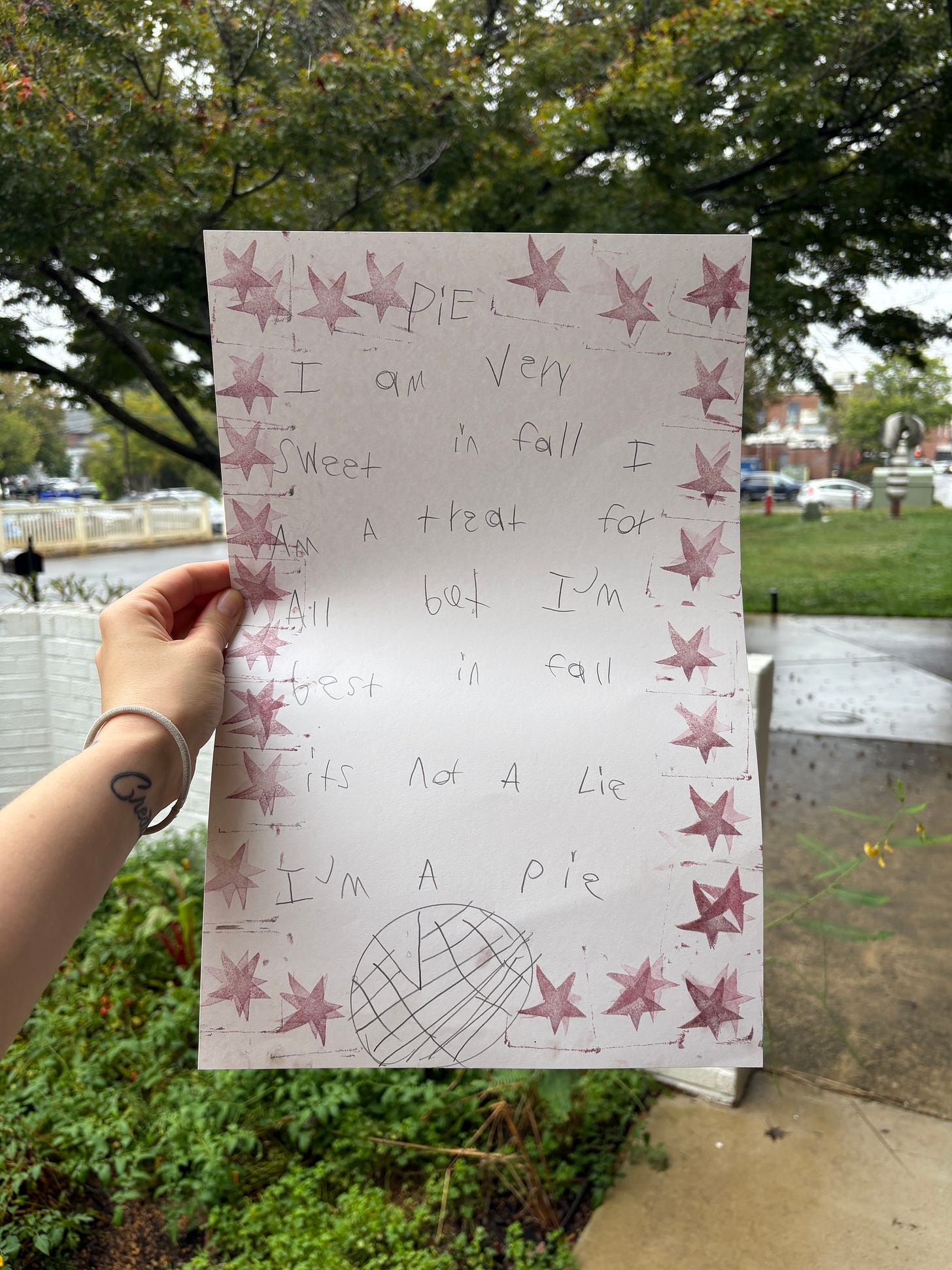 Shady holding a students handwritten poem with stamps of brownish-purple stars and a pen drawing of a pie.