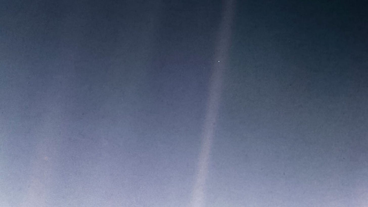 In the image, Earth appears as a tiny, faint blue speck within a scattered ray of sunlight, occupying less than a pixel in the photograph. This perspective underscores Earth’s minuscule size in the vastness of space