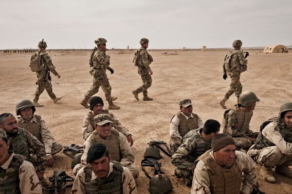 Troops standing and seated on a barren plain.