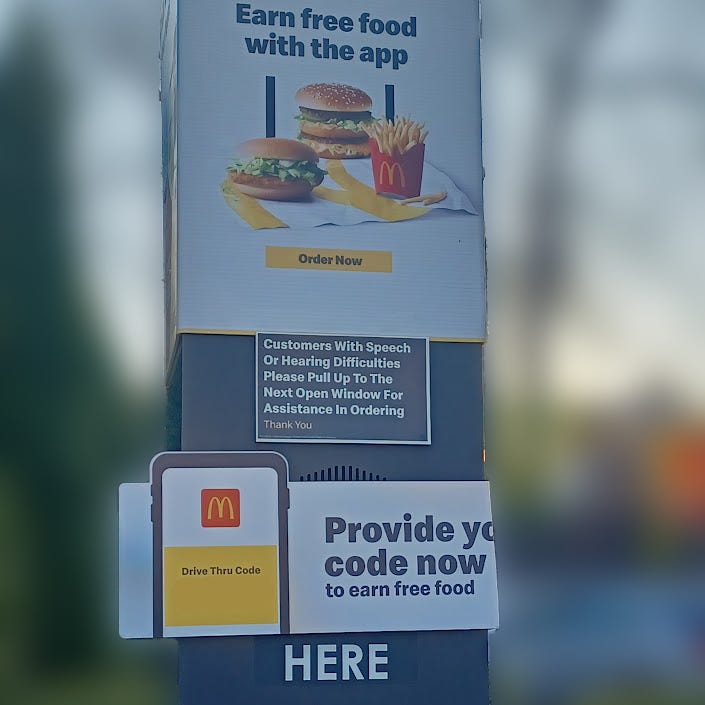 Pillar with signage in a fast food drive thru that instructs customers with speaking or hearing difficulties to please pull up to the next open window for assistance in ordering