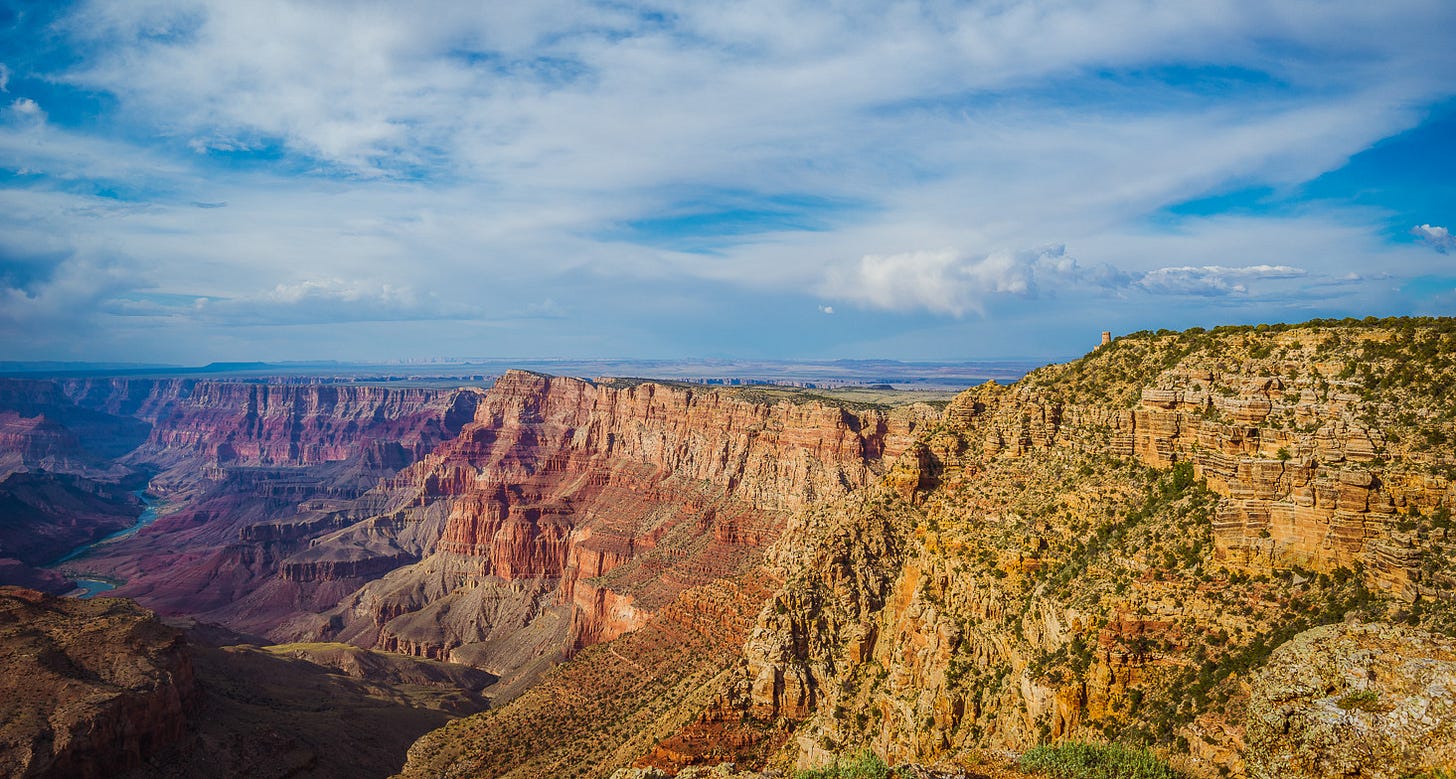 Colorful canyon walls below a blue sky with sweeping white clouds.