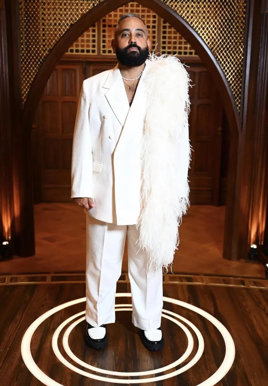 Yam Yam in an oversized white double-breasted suit with a long white ostrich feather stole draped over one shoulder, black and white loafers.