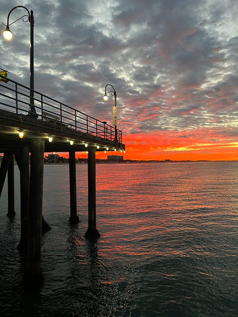 the pier sign, the pacific park sign, the end of route 66 sign, and the sun setting and rising over the pier