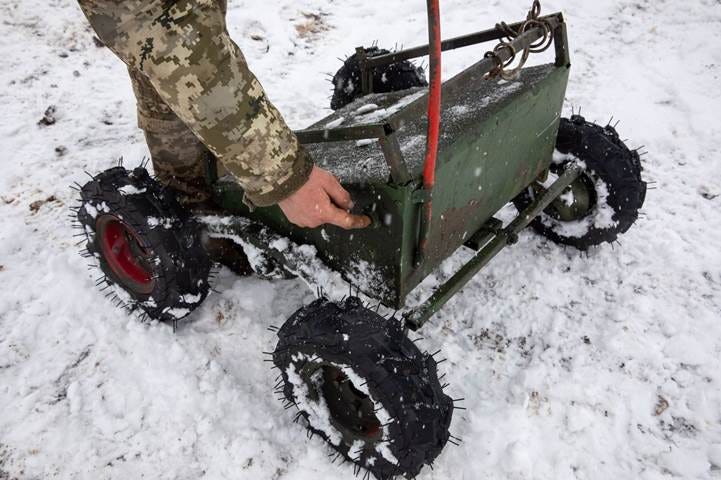 A person pushing a green cart in the snow

Description automatically generated