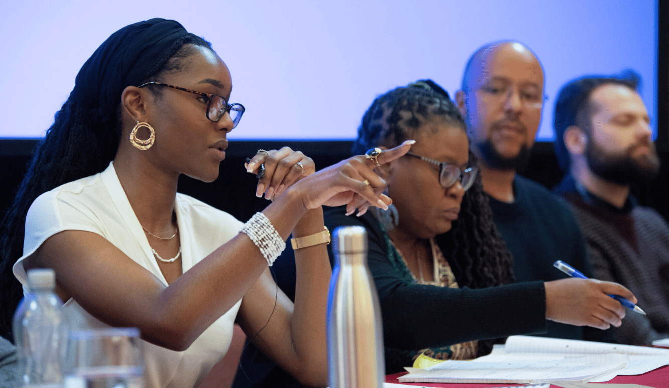 A young African woman with glasses and headscarf points at audience and speaks into microphone. A young African woman with glasses and headscarf points at audience and speaks into microphone.