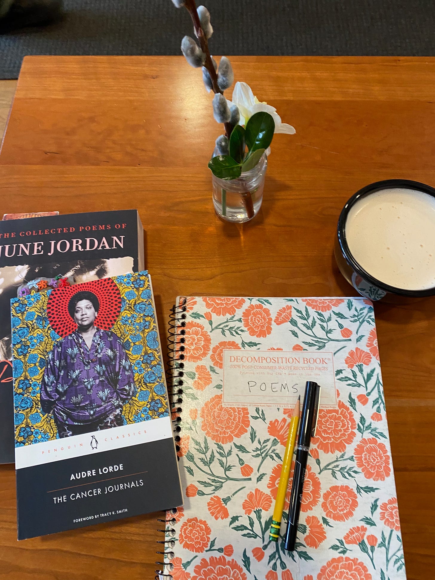 The Cancer Journals, the poetry of June Jordan, and a notebook on a cafe table next to a vase of pussy willow and a London fog.