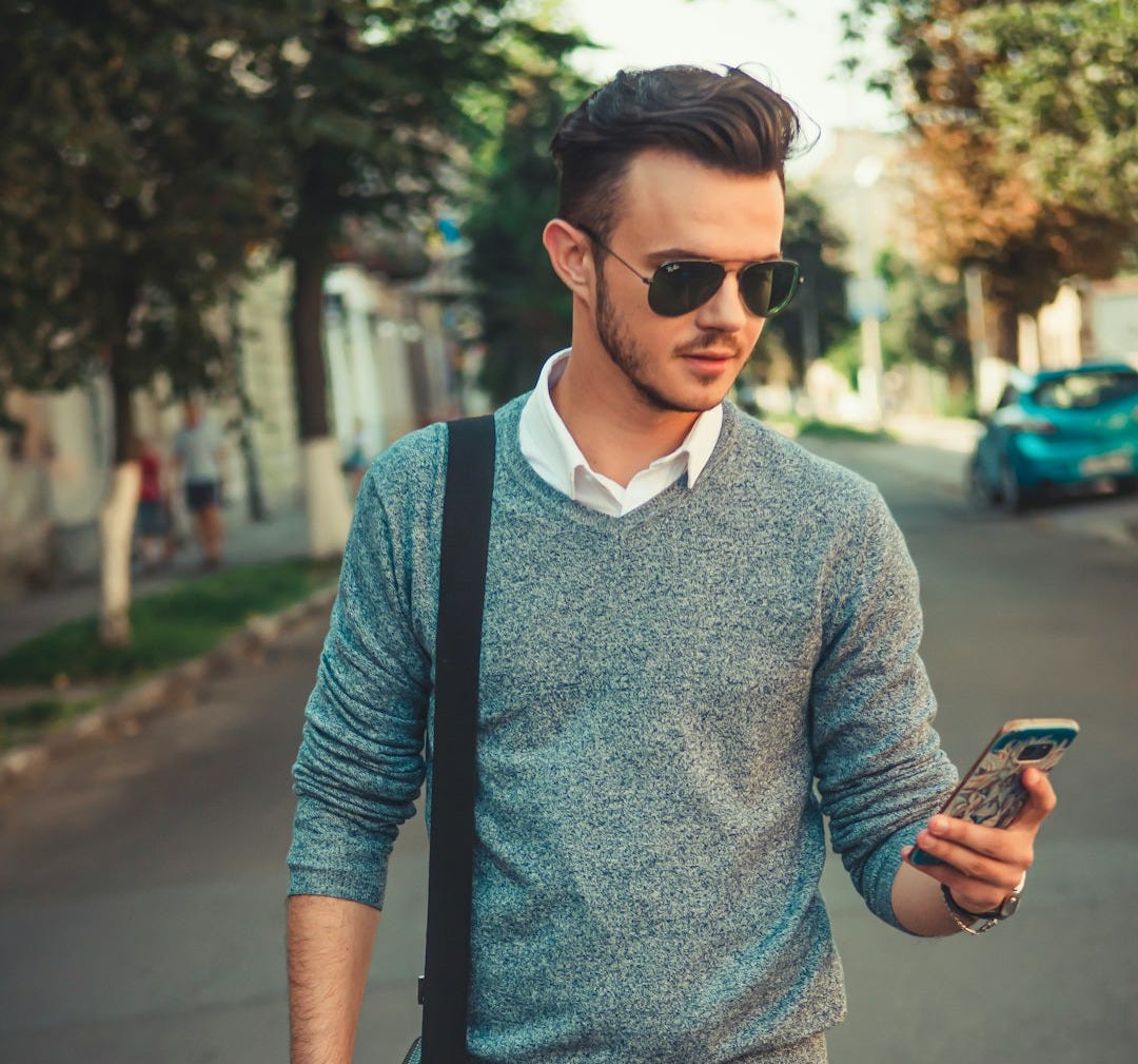 man in blue and gray polo shirt holding black smartphone man in blue and gray polo shirt holding black smartphone