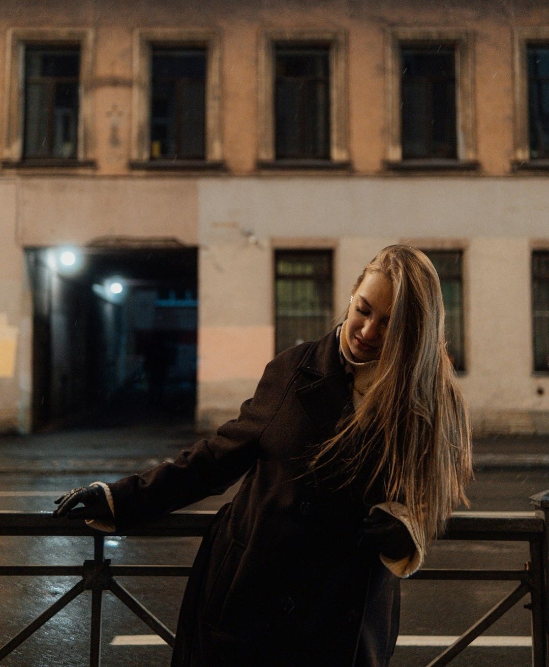 Woman leaning on railing in front of building at night