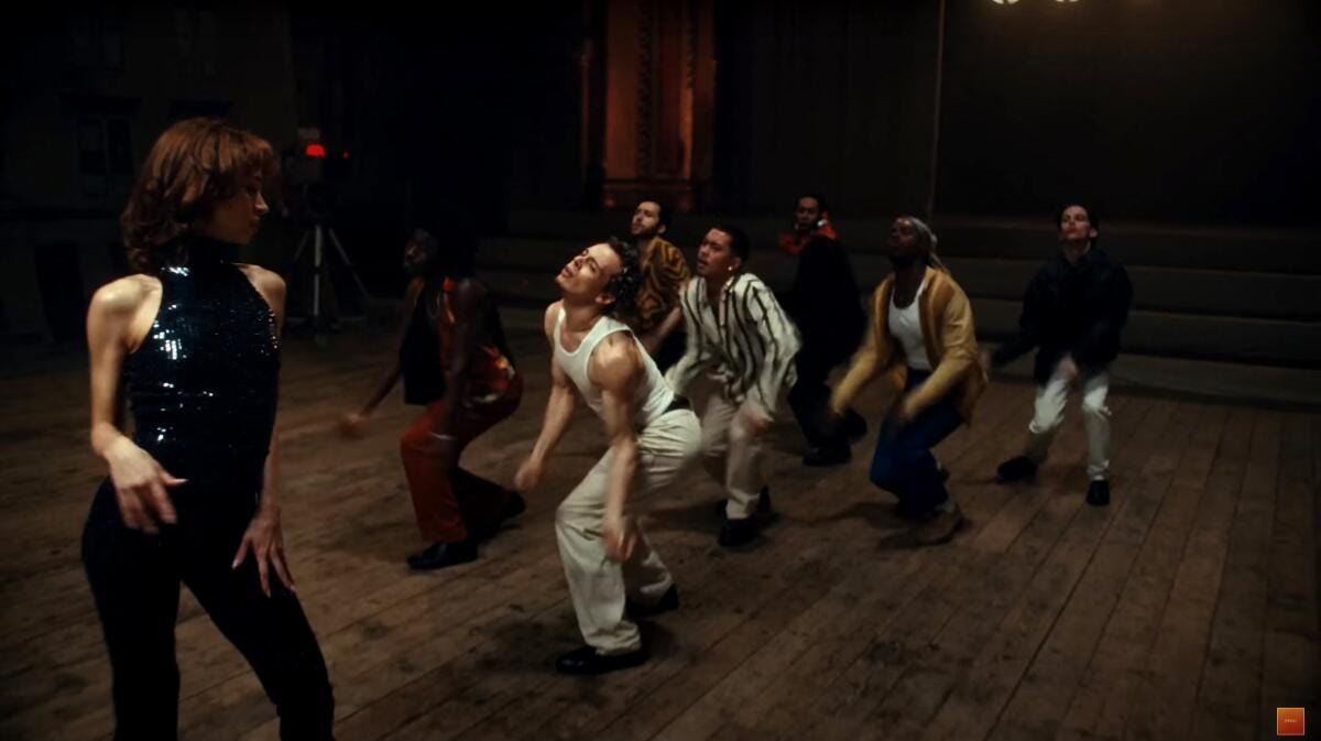 Male dancers moving towards a woman in black