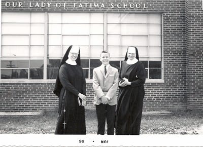 Black-and-white photo of two nuns in habits and a boy in a suit standing and smiling in front of a brick building labeled Our Lady of Fatima School. The photo appears to be from June 1966.