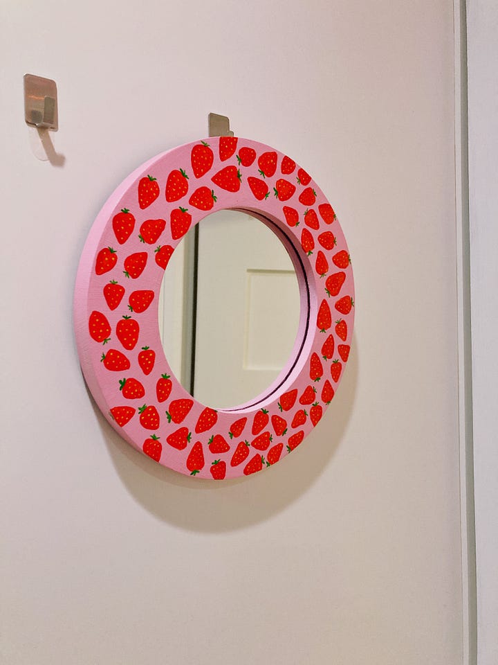 One mirror has stacks of donuts around the frame and the other is pink with strawberries painted all around the frame.
