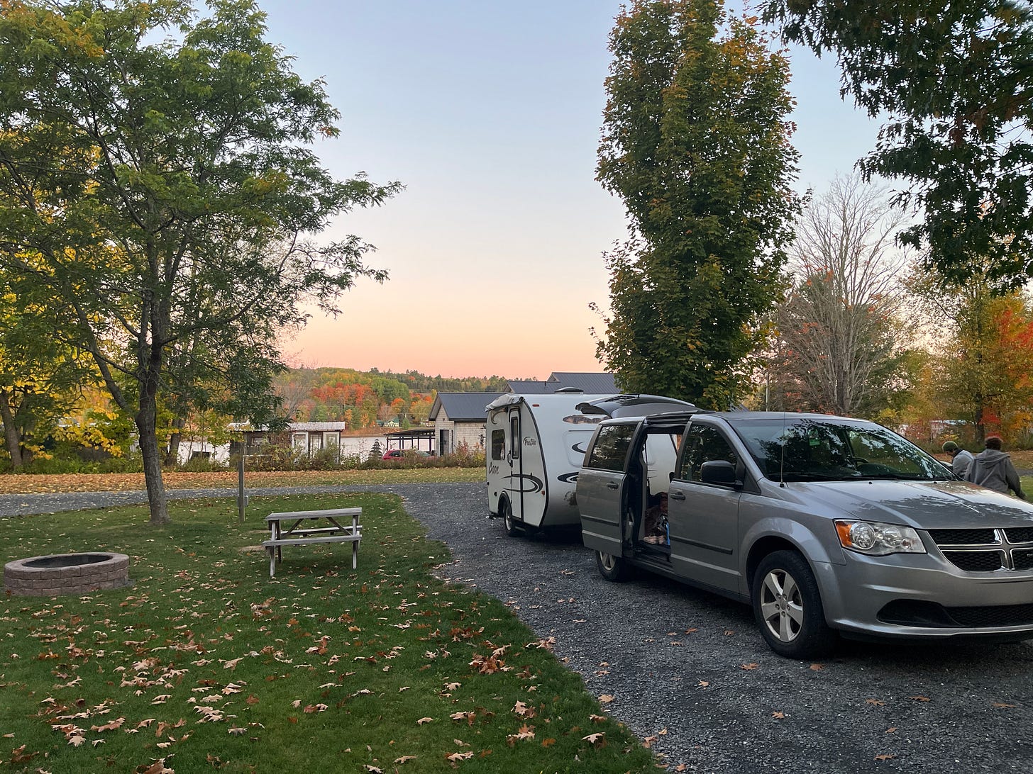 Our mini van and small white camper parked at a campground overlooking the St. John River with the colour of autumn leaves all around