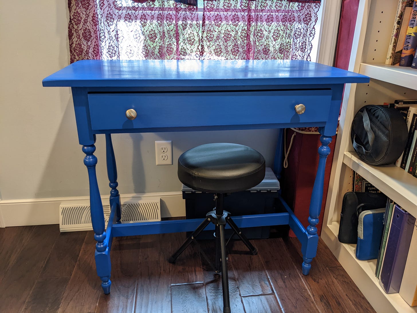 A blue table with silver drawer pulls sits to the left of a bookshelf. A blue table with silver drawer pulls sits to the left of a bookshelf.