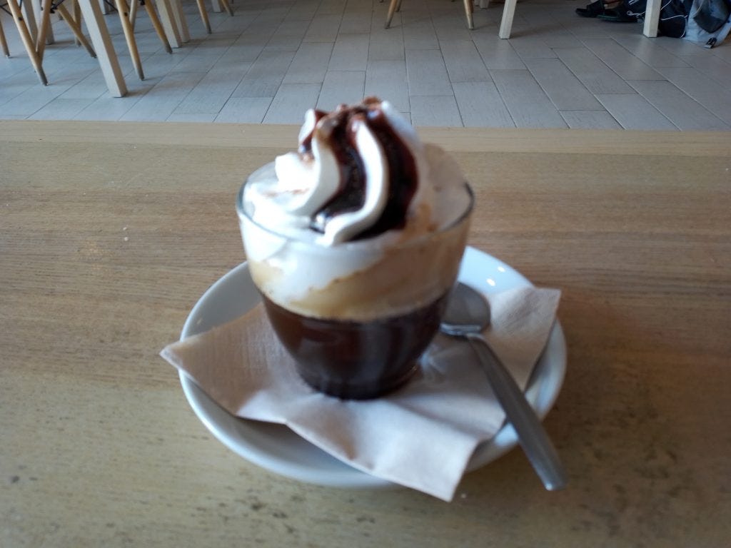Layered mochaccino coffee drink in a clear glass, dark coffee on the bottom, LOTS of whip cream, and chocolate sauce on top. Yummy. And CAFFEINE! 