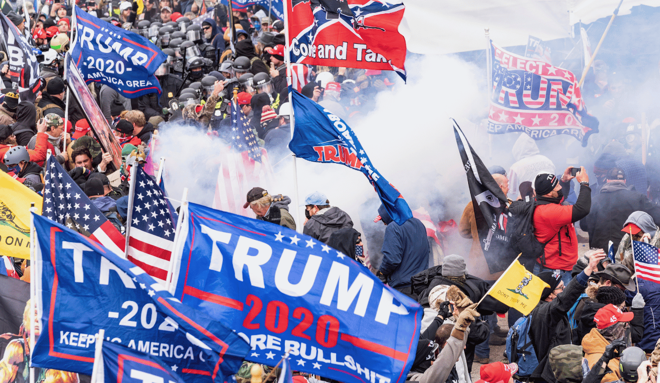 Crowd of protesters waving Trump 2020 flags amid police lines and smoke during unrest outside the US Capitol. Crowd of protesters waving Trump 2020 flags amid police lines and smoke during unrest outside the US Capitol.