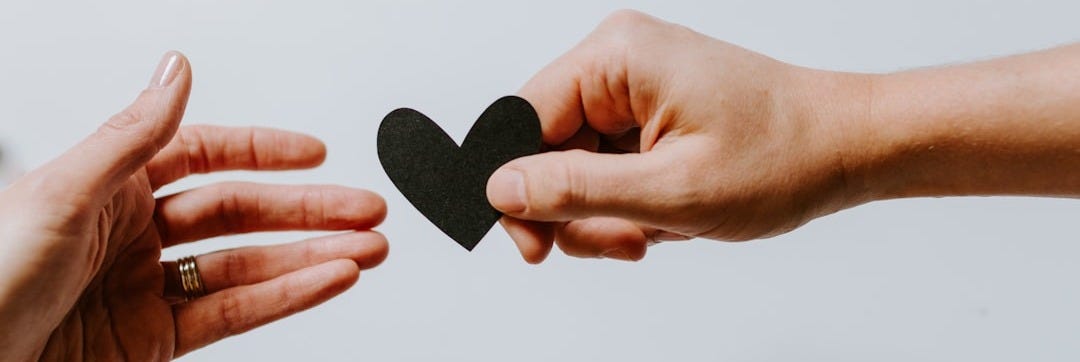 person reaching black heart cutout paper