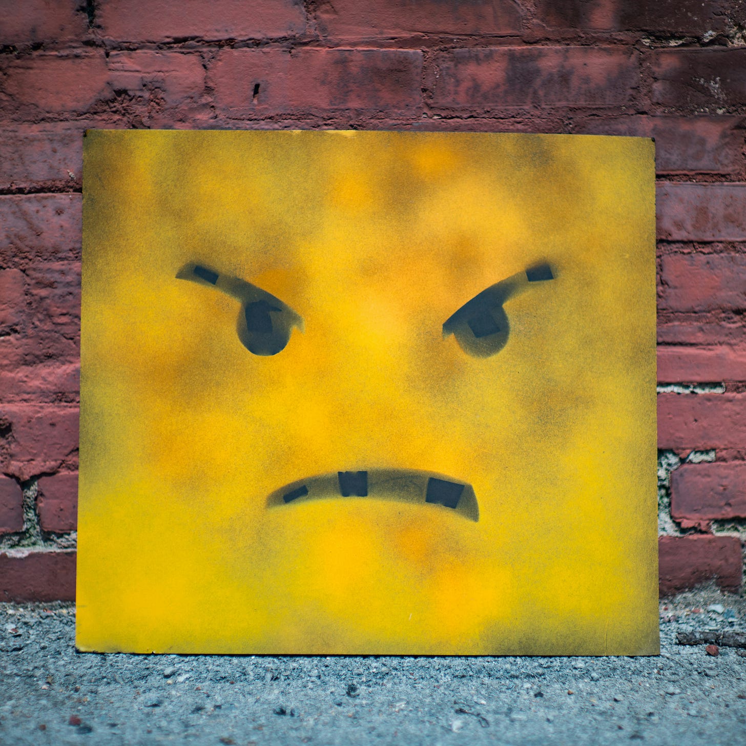 Angry face emoji sculpture against a brick wall.